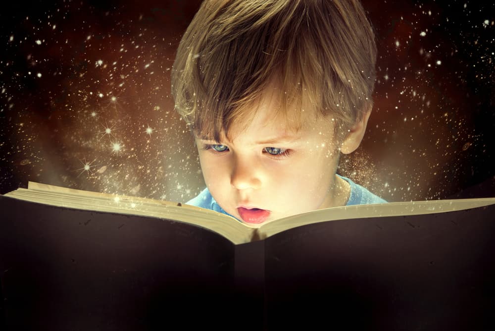 Little boy with a love of reading, enjoying a book with glowing fairy dust coming out of it.