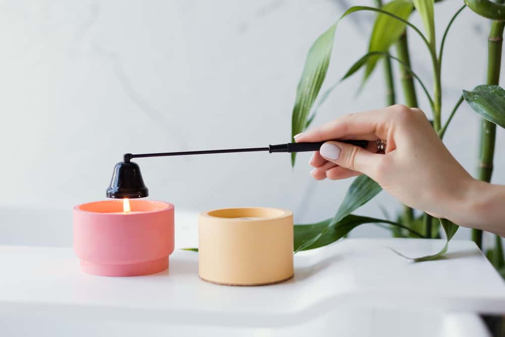 Craft pink and orange soy candles on baththube near bamboo plant at white light bathroom interior. Woman extinguish candle with black candle snuffer