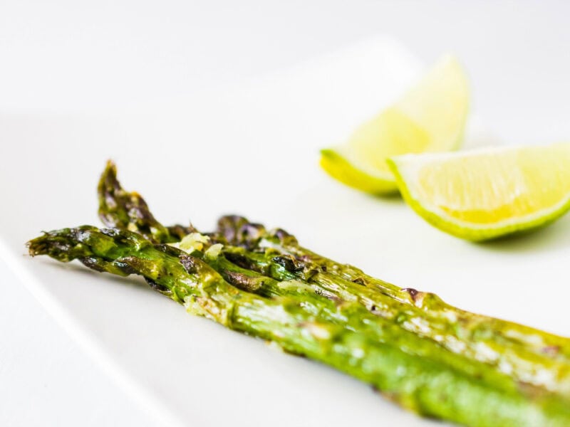 Roasted asparagus on a white background with lemon wedges.