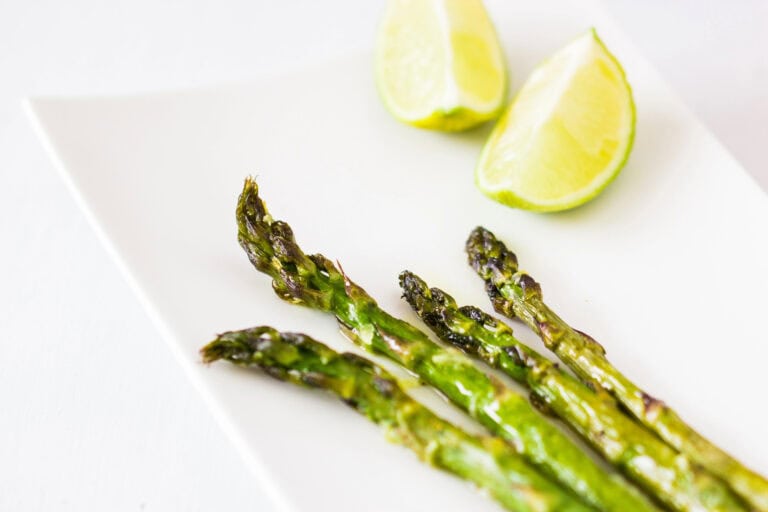 Roasted asparagus on a white background with lemon wedges.